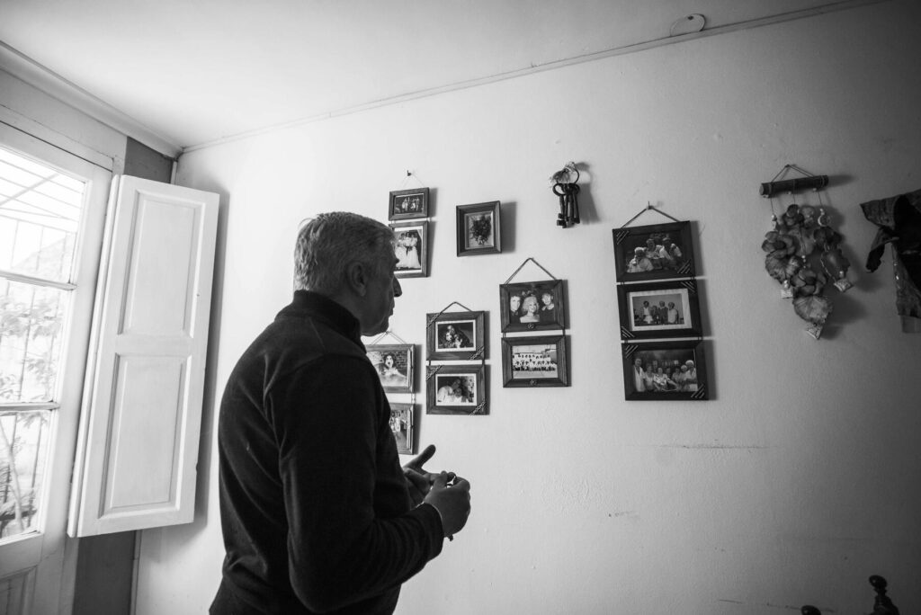 Imagen en blanco y negro, señor observando cuadros familiares en la pared.