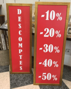 Dos carteles verticales rojos con moldura dorada fabricados por ContellMarcs Barcelona, uno con la palabra "Descomptes" en letras blancas y otro con descuentos del 10% al 50%, impresos en digital y montados sobre forex.