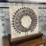 Vitrina cuadrada de metacrilato transparente fabricada por Contell Marcs que protege y expone una corona o aureola religiosa antigua de filigrana metálica plateada sobre peana de madera oscura, ante pared de azulejos tradicionales.
