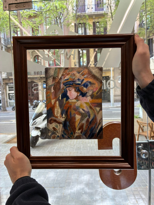 Técnico de ContellMarcs sostiene frente a un escaparate de Barcelona un marco de madera nogal con montaje al aire y doble cristal que enmarca una pintura figurativa cubista de mujer con sombrero.