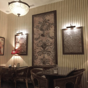 Interior de café clásico en Barcelona decorado con tapiz y cuadros enmarcados por Contell Marcs, molduras de madera oscura envejecida con iluminación cálida sobre pared a rayas, proyecto de decoración con marcos para hostelería.