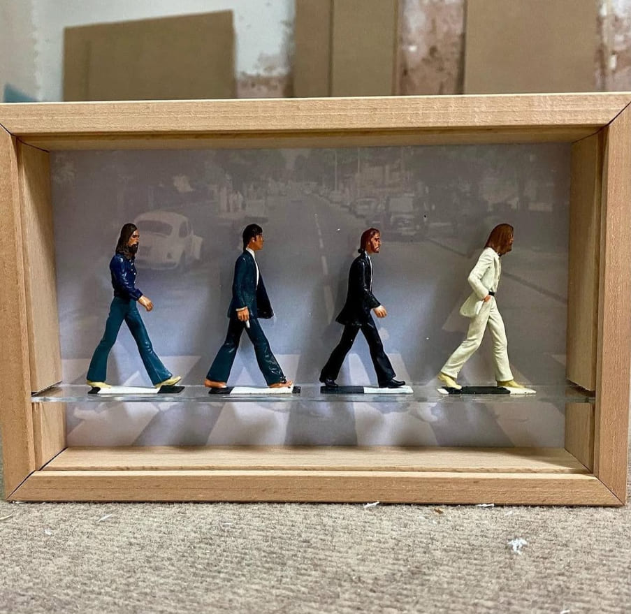 Vitrina diorama terminada por Contell Marcs con marco de madera natural, cuatro figuras de músicos en miniatura sobre paso de cebra y fotografía en blanco y negro como fondo, trabajo artesanal personalizado.