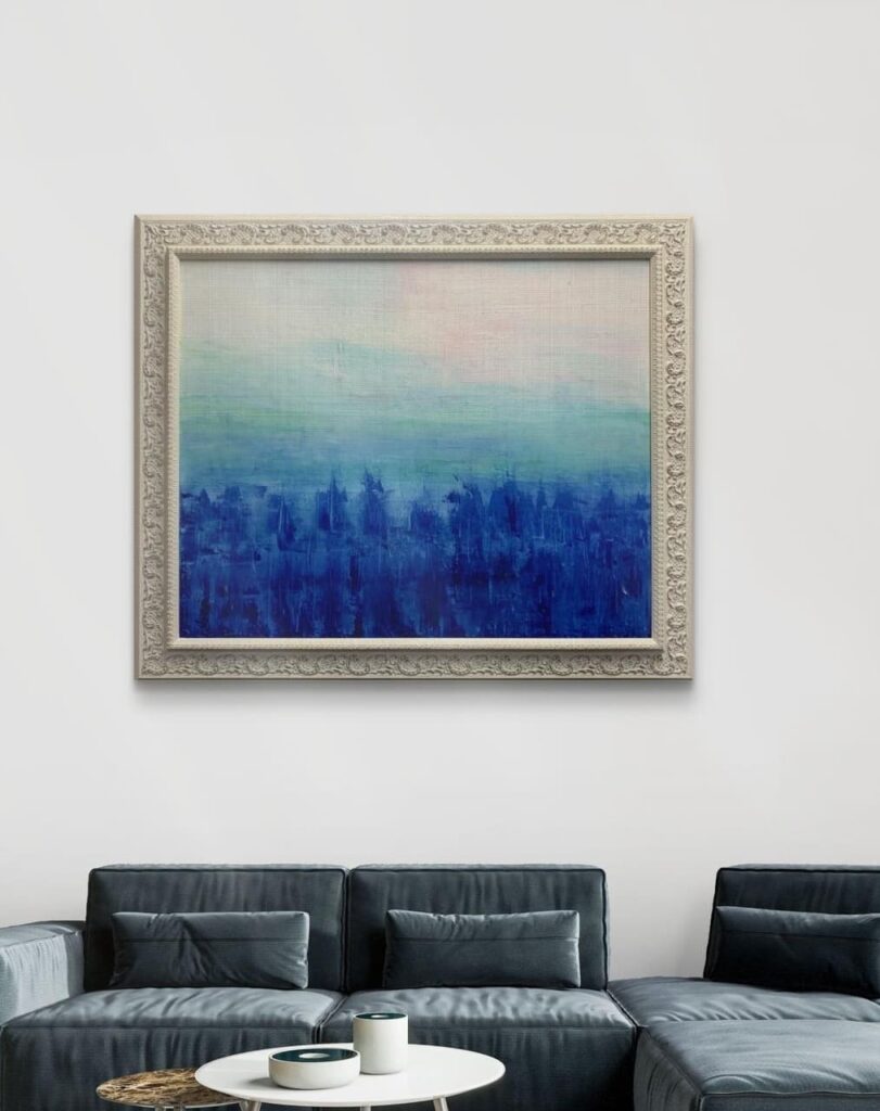 Pintura abstracta en tonos azul marino y celeste enmarcada con marco de madera blanco tallado con motivos florales, colgada sobre sofá gris en salón moderno por Contell Marcs.
