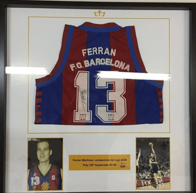 Marco vitrina a medida con camiseta de baloncesto azulgrana número 13 firmada de Ferran Martínez del FC Barcelona, acompañada de dos fotografías del jugador y placa identificativa de la temporada 89-90 de la Liga ACB, trabajo de enmarcación deportiva realizado por Contell Marcs.