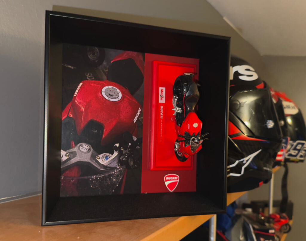 Marco vitrina negro de profundidad con moto Ducati en miniatura a escala montada sobre fondo rojo, junto a fotografía de detalle de la moto real, trabajo de enmarcación personalizada para coleccionista realizado por Contell Marcs.