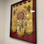 Marco vitrina negro de gran formato con fondo rojo que conserva y expone un estandarte religioso bordado en dorado y amarillo con inscripción Corpus Christi, trabajo de enmarcación especial para pieza textil histórica realizado por Contell Marcs.