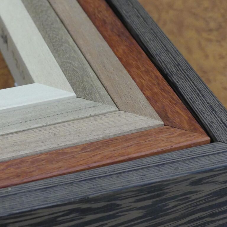 Primer plano de la esquina de cuatro marcos de madera lisos apilados en tonos naturales: blanco, gris piedra, caoba rojizo y negro veteado, mostrando la calidad del acabado y la veta de la madera, de Contell Marcs.