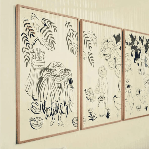 Tríptico de tres ilustraciones en tinta azul y negra sobre fondo crema con motivos orientales de figuras y vegetación, enmarcadas con marcos de madera natural de roble de perfil fino, instaladas en serie en pared clara, trabajo realizado por Contell Marcs.